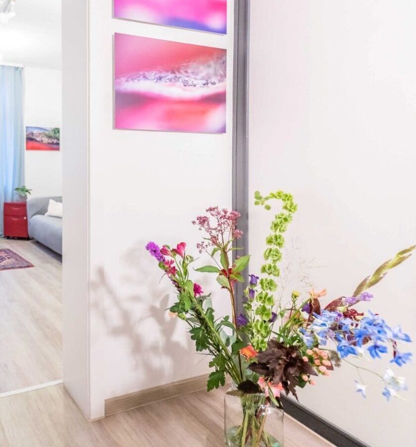 Offene Zimmertür zur Lehrpraxis, Bodenvase mit bunten Blumenstrauß und Kunstwerke an der Wand